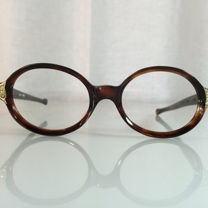 May include: A pair of tortoiseshell oval-shaped eyeglasses with gold accents and rhinestones on the temples.