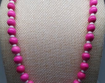 Puede incluir: Un collar de cuentas rosas con espaciadores blancos y una cadena plateada. Un colgante ovalado blanco con las palabras "Beach Girl" cuelga del collar. El collar se exhibe en un maniquí.
