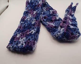 Puede incluir: Una bufanda tejida a ganchillo a mano con un patrón de hilo jaspeado en tonos azul marino profundo, azul real, bígaro claro y morado oscuro. El accesorio está elaborado con un patrón de punto abierto y texturizado de tela suave.