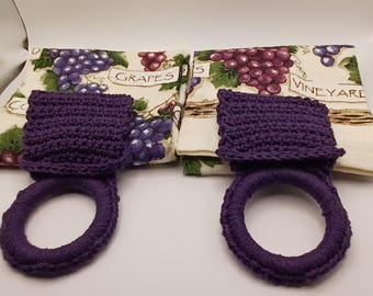 Puede incluir: Dos paños de cocina con estampado de uvas y viñedos con el texto GRAPES y VINEYARD, cada uno combinado con una parte superior de ganchillo morado oscuro y un anillo de ganchillo morado oscuro a juego para colgar el conjunto de accesorios.