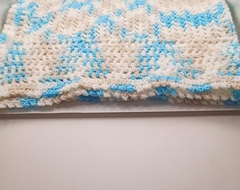 Puede incluir: Una manta rectangular tejida a mano que presenta un patrón variado de hilo blanco suave y azul cielo brillante. El tejido muestra una construcción de punto abierto consistente con una apariencia texturizada y en bucle en toda la superficie.