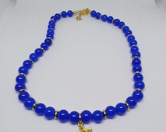 Puede incluir: Un collar de cuentas azules con detalles dorados y un colgante de estrella de mar dorado. El collar presenta cuentas azules redondas y brillantes y pequeños espaciadores dorados. El cierre también es dorado. Una joya elegante.