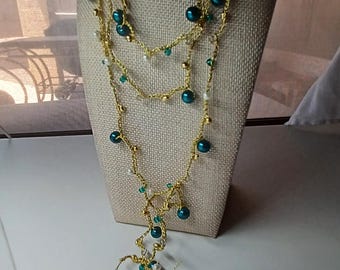 Puede incluir: Collar de varias hebras exhibido en un maniquí. El collar presenta cadenas doradas adornadas con cuentas de color turquesa, blancas y doradas. El collar es de varias capas y tiene un diseño en cascada.