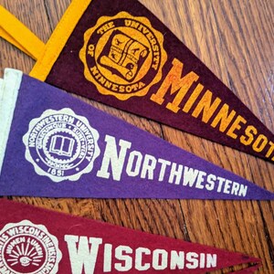 May include: Three vintage pennants in maroon, purple, and red. The maroon pennant reads "THE UNIVERSITY OF MINNESOTA". The purple pennant says "NORTHWESTERN". The red pennant says "WISCONSIN". Each pennant has a white border and a loop for hanging.