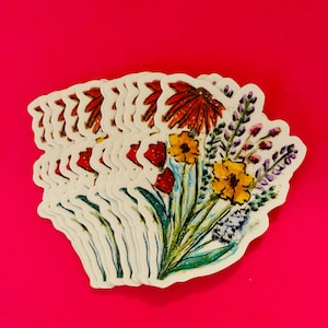May include: A stack of floral stickers featuring a watercolor design of various flowers in shades of red, yellow, purple, and green. The stickers are on a bright pink background.