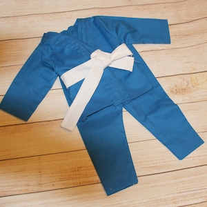 Op de afbeelding: Een blauw karatepak met een witte band. Het pak is gemaakt van een zachte, comfortabele stof en is perfect voor martial arts training.