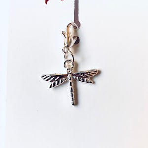 Peut inclure: Breloque en forme de libellule argentée avec un fermoir argenté. Le charme est sur une carte blanche avec un diable rouge et un ange bleu en haut et le texte "heavenlyhellelements@msn.com" et "Heavenly Hell Elements" en bas.