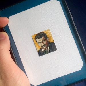 May include: A framed miniature painting of a man with a mustache and a dark suit. The painting is on a white background and has a blue mat. The artist's signature, "OBETSY MARSCH", is visible in the lower right corner.