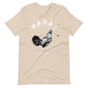 May include: A tan t-shirt with a black and white illustration of a rooster. The text "Kauai - The Garden Isle" is above the rooster. The text "Aloha Kekoa" is to the left of the rooster and the text "Shaka doodle doo!" is below the rooster.