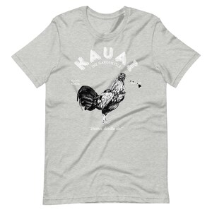 May include: A grey t-shirt with a white graphic of a rooster and the text "Kauai - The Garden Isle" with the words "Aloha Kekoa" and "Hawaii" on either side of the rooster. The text "Shaka doodle doo!" is below the rooster.