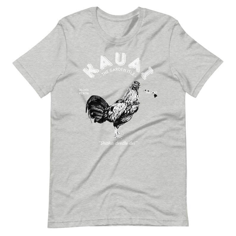 May include: A grey t-shirt with a white graphic of a rooster and the text "Kauai - The Garden Isle" with the words "Aloha Kekoa" and "Hawaii" on either side of the rooster. The text "Shaka doodle doo!" is below the rooster.