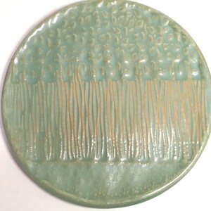 May include: A light green ceramic plate with a raised design of a row of trees with leaves on top. The plate is oval shaped.