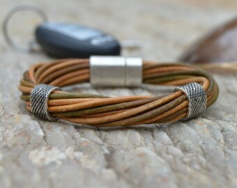May include: A braided leather bracelet with a magnetic clasp and silver accents. The bracelet is made of brown and green leather.