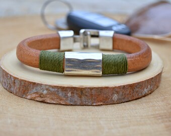May include: A brown leather bracelet with a silver metal accent and green cord accents.
