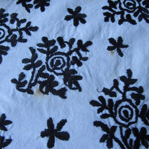 May include: A white fabric background with black embroidered floral designs. The designs are intricate and detailed, featuring a variety of flower shapes and sizes.