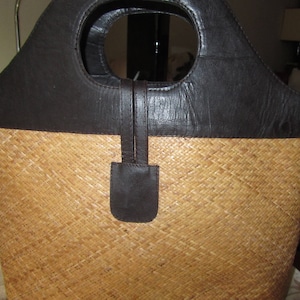 May include: A brown leather and woven straw tote bag with a top handle. The bag has a flap closure and a brown leather strap.