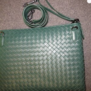Puede incluir: Un bolso de hombro de cuero tejido verde oscuro con una correa larga y un cierre de solapa. El bolso tiene un patrón tejido y un acabado de cuero liso.