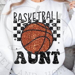 May include: White sweatshirt with a black and orange basketball graphic and the text "Basketball Aunt" in black.