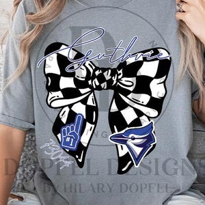 May include: Gray t-shirt featuring a large black and white checkered bow with the word "Guthrie" in blue script. Accompanying the bow are a blue #1 hand and a blue and white bird logo. The number "73044" is also visible.