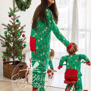 May include: A woman and a child wearing matching green and red pajamas with a Nutcracker print. The child is riding a red tricycle with a white handlebar. The woman is smiling and looking at the child. There is a small Christmas tree and a wreath in the background.