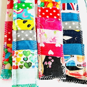 以下が含まれることがあります： パッチワークデザインの手作り布製ブックマーク。各ブックマークは、水玉模様、花柄、ハートなど、カラフルな模様の生地のユニークな組み合わせが特徴です。エッジはジグザグステッチで仕上げられています。