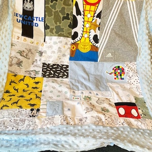 Op de afbeelding: Een patchwork quilt met verschillende stoffen vierkanten. Ontwerpen omvatten een Newcastle United voetbalshirt, camouflage, een Woody uit Toy Story ontwerp en een Adidas logo. De quilt is afgezet met een lichtblauwe, getextureerde stof.