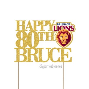 May include: Gold glitter cake topper with the text "Happy 80th Bruce" and a Brisbane Lions logo.