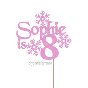 May include: Pink glitter cake topper with the name "Sophie is 8" and snowflakes.