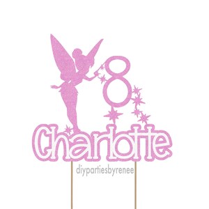 May include: A pink glitter cake topper with a fairy silhouette, the number 8, and the name "Charlotte". The fairy is holding a wand, and stars trail from the number 8. The text "diypartiesbyrenee" is at the bottom.