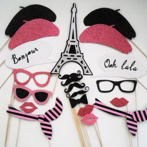 May include: A set of 10 photo booth props with a Parisian theme. The props include a black beret, a pink beret, a black and white Eiffel Tower, a pair of black glasses, a pair of pink glasses, a black moustache, a black bow tie, a pink scarf, a speech bubble that says "Bonjour", and a speech bubble that says "Ooh la la".