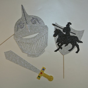 May include: Three silver glitter photo booth props: a knight's helmet, a sword, and a knight on horseback with a shield.