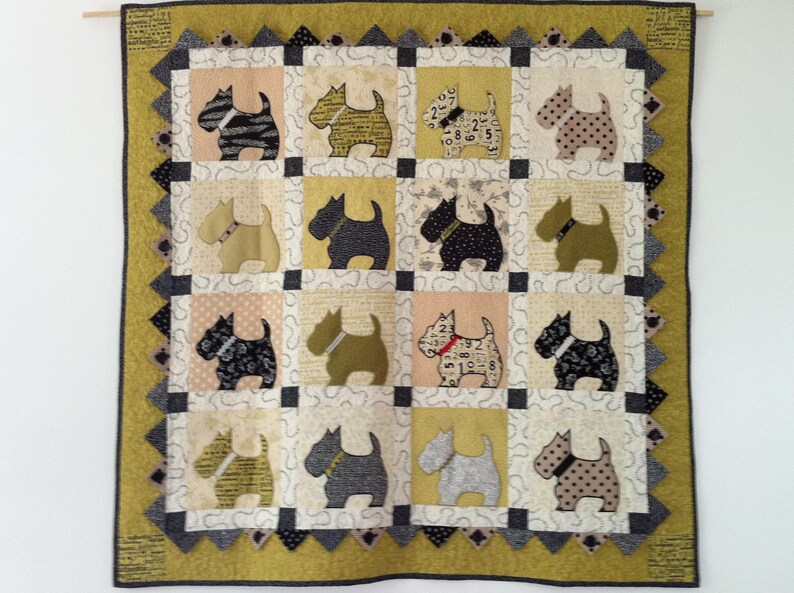 Op de afbeelding: Een handgemaakte quilt met een herhalend patroon van terri&euml;r honden applicaties. De honden zijn in verschillende kleuren en patronen, tegen een patchwork achtergrond van neutrale tinten. De quilt heeft een decoratieve rand in groen- en grijstinten.