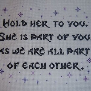 May include: Cross-stitch embroidery with purple stars and black text that reads "Hold her to you. She is part of you, as we are all part of each other."