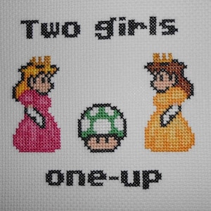 May include: Cross-stitch embroidery featuring two princesses from the Super Mario Bros. video game series, with the text "Two girls one-up" above them.
