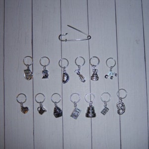May include: A set of 14 silver-toned stitch markers with various baking-themed charms, including a cupcake, a whisk, a cake, and a heart. A silver safety pin is also included.
