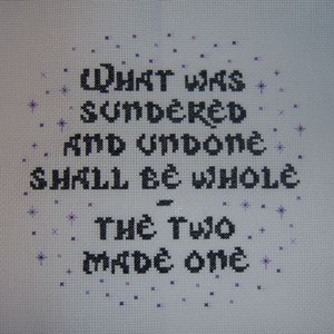 May include: Cross-stitch embroidery with black thread on white fabric. The text reads "What was sundered and undone shall be whole - the two made one".