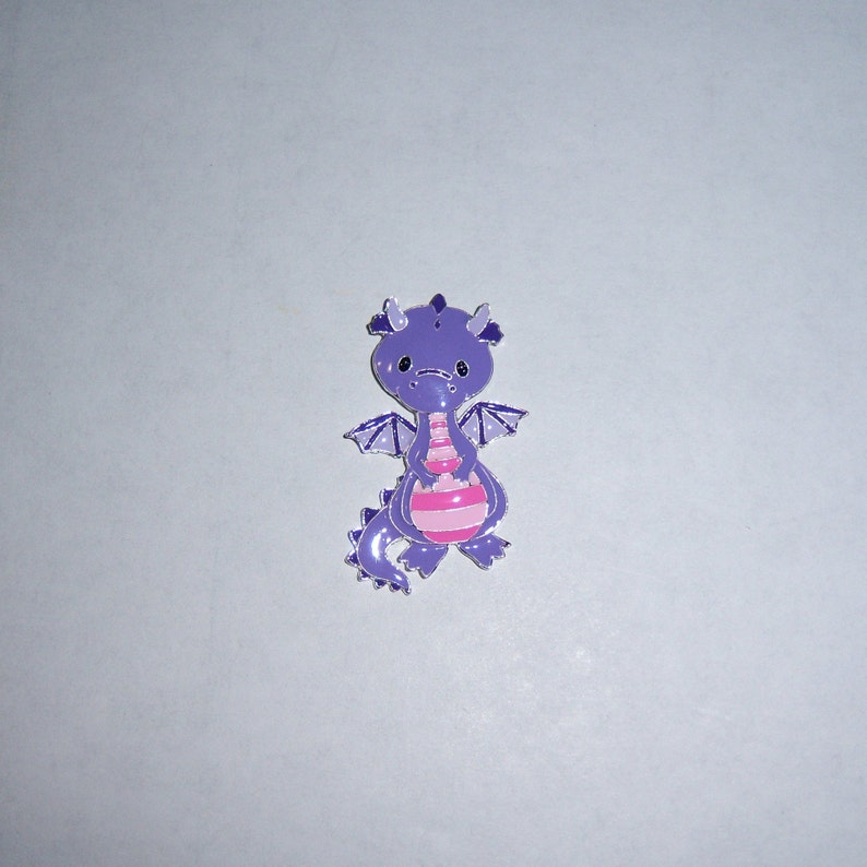 May include: Purple dragon charm with pink stripes and wings. The dragon is holding a pink ball in its front paws.