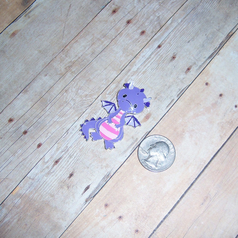 May include: Purple and pink cartoon dragon charm with a white background.