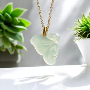 May include: A delicate jade pendant necklace featuring a carved butterfly design. The pendant is a light green color and is suspended from a gold chain.