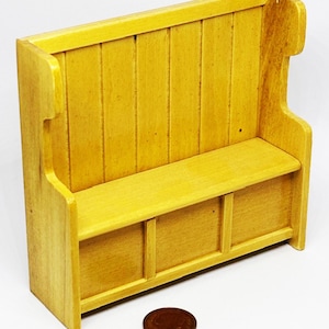 May include: A miniature wooden bench painted in a light yellow hue. The bench features a backrest with vertical planks, a seat, and a lower section with three compartments. The design is simple and rustic, suitable for a dollhouse or miniature setting.