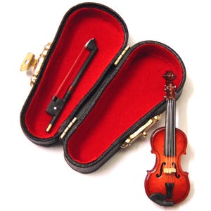 Könnte beinhalten: Eine Miniaturvioline mit einem braunen Holzkörper und einem schwarzen Etui. Die Violine hat eine rotbraune Oberfläche und ist mit schwarzen Linien verziert. Das Etui ist mit rotem Samt ausgekleidet und hat einen goldfarbenen Verschluss.