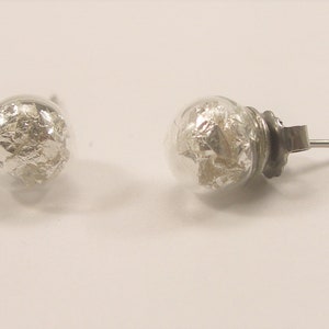 Peut inclure: Une paire de boucles d'oreilles en argent avec des boules de verre transparentes remplies de paillettes argentées.