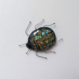 May include: A glass bug sculpture with a black, blue, and gold iridescent finish. The bug has six wire legs.