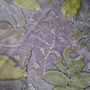 May include: A close-up of a light purple fabric with a green leaf pattern. The leaves are in various shapes and sizes, and they are arranged in a random pattern. The fabric has a soft, flowing texture.