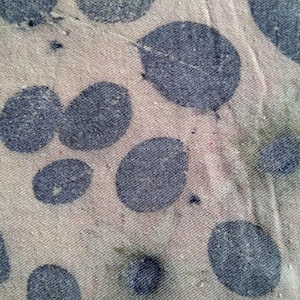May include: Close-up of a beige textile featuring a pattern of large, dark blue leaf imprints. The fabric has a slightly worn appearance, with visible texture and subtle colour variations.