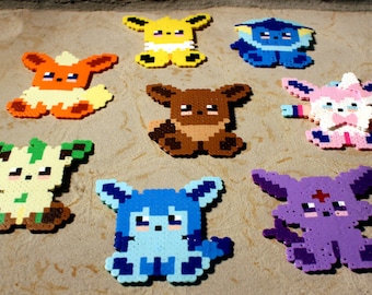 May include: Nine colorful pixel art Pokemon characters, including Eevee, Vaporeon, Jolteon, Flareon, Espeon, Umbreon, Leafeon, Glaceon, and Sylveon. Each character is made of small plastic beads.