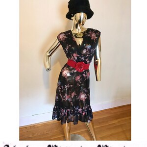 May include: A black floral print dress with a red belt and a black hat. The dress has a V-neckline and a ruffled hem.