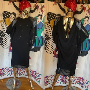 May include: A black, long-sleeved dress with a cowl neck and sequined shoulder accents. The dress is on a mannequin with a red hat.