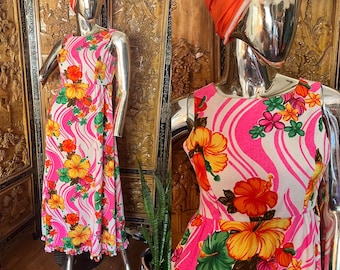 May include: A sleeveless, floor-length dress with a vibrant floral print. The dress features a white background with pink wavy stripes and colorful hibiscus flowers in yellow, orange, and red. The dress is displayed on a mannequin.