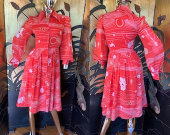 May include: A red vintage dress with a white and gold abstract print. The dress has a collared neckline, long sleeves, and a button-up front.